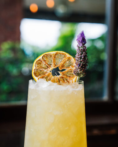 Closeup of yellow cocktail topped with dried orange and lavender