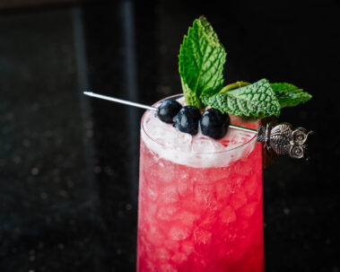Closeup of pink cocktail topped with blueberries and mint sprigs