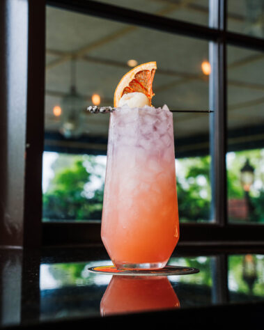 Orange and purple ombre cocktail topped with dried orange slice and lychee