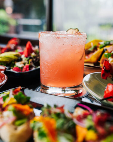 pink/orange cocktail with food plates out of focus